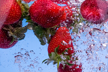 Strawberries in water with water splash and air bubbles on blue background. Close up image.