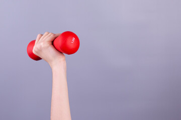 Girl 's hand holding red dumbbell on grey background. concept.  Sport and healthy lifestyle concept with Copy space.