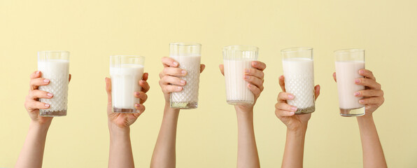 Female hands with glasses of vegan milk on yellow background - obrazy, fototapety, plakaty