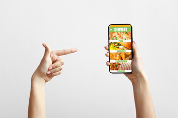 Hands of young woman with smartphone ordering food online on light background