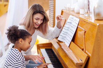 Woman and girl playing a piano. Beautiful mom teaching her daughter playing a piano. The piano...