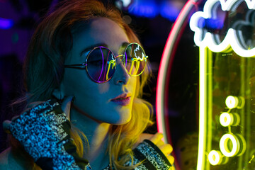 Long hair girl with sunglasses and leather jacket looking at neon lights - obrazy, fototapety, plakaty
