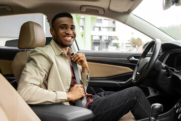 Portrait of an afro american man sitting in the driver's seat of a car and wearing a seat belt for safety