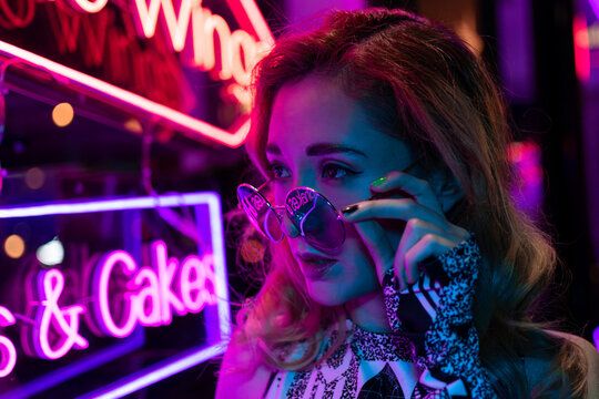 Toned portrait of beautiful young woman near neon lighting on wall
