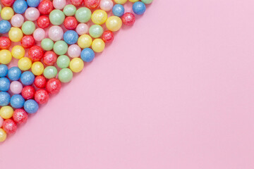 Multi-colored round glossy balls of sugar confectionery lie diagonally to the left on a pink background.