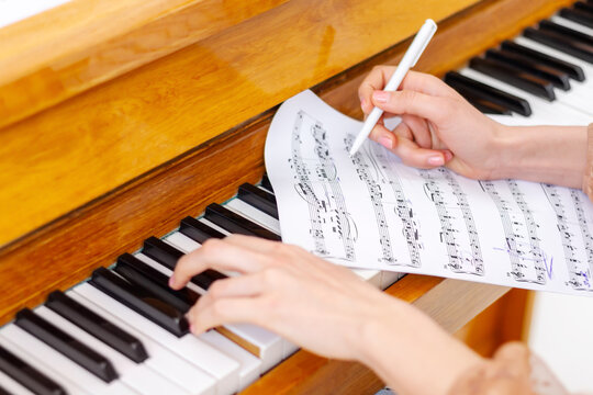 Woman's hands playing piano at home. The woman is professional pianist arranging music using piano keyboards. Musician practicing keyboard composing music. Artist create instrumental acoustic melody.