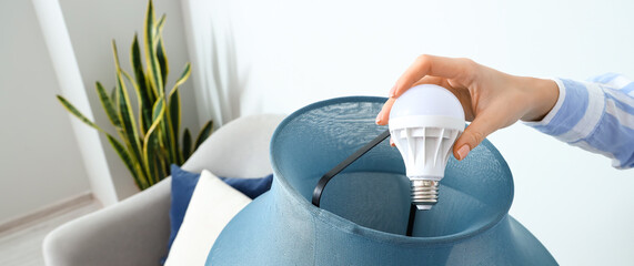 Woman changing light bulb of standard lamp at home