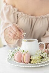 Traditional delicious French dessert - sweet homemade macarons on a vintage plate. Colourful tasty macaroons served on a white china with herbal tea. Decorated with fragile cherry tree flowers.