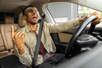 Joyful afro american man dancing in car, singing while driving his car. Road fun