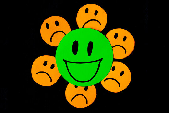 image of some emoticons cut out of orange paper with a sad face surrounding a big green emoticon with a smiling face. concept of bad influences, bad friendships, negativity, problems, bullying...