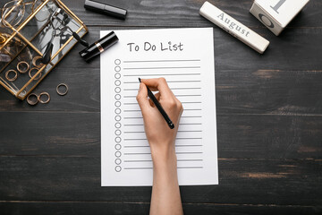 Female hand with to-do list, cosmetics and accessories on dark wooden background