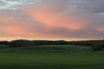 Peaceful landscape with pink dusk clouds and green fields - 508324049