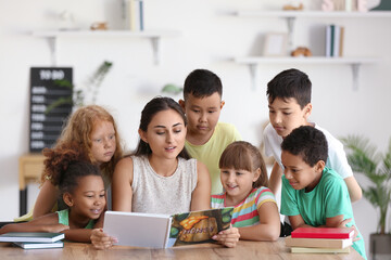 Little children having literature lesson with their teacher in classroom