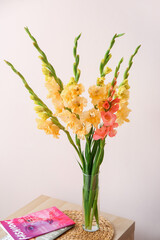 Vase with beautiful gladiolus flowers and magazines on table in room, closeup