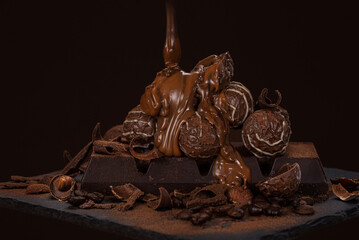 Heap of dark chocolate and chocolates covered with chocolate icing on a black background.
