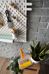 Stepladder stool with paint roller, houseplant and pegboard with decorator's tools on grey brick wall