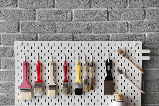 Pegboard With Decorator's Tools On Grey Brick Wall, Closeup