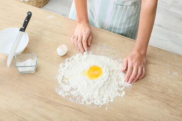 Young woman making dough on table in kitchen, closeup