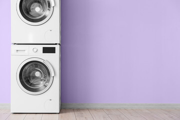 Modern drying and washing machines near violet wall in room