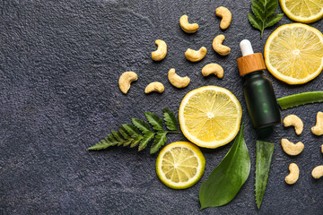 Bottle of natural serum with lemon slices, plant leaves and cashew nuts on dark background