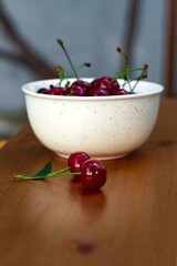 Two fresh ripe juicy organic cherries on a brown wooden table and a white bowl with cherries in the background