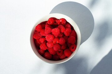 Fresh sweet organic raspberries in white bowl on white background with contrast shadow