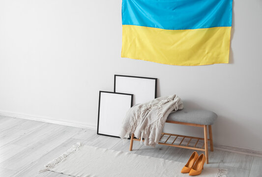 Bench with plaid, blank photo frames and flag of Ukraine hanging on white wall