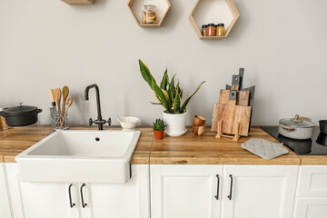 Fototapeta na wymiar White counters with sink, food, kitchen utensils and houseplants near light wall