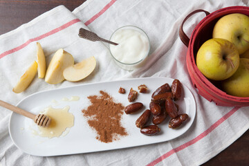 sliced apples, whole apples, honey, yogurt, cinnamon and dates laid out on a kitchen towel