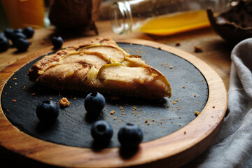 apple pie on a black round plate with blueberries on a table with orange juice bottle ..