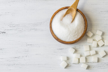 Heap of white granulated sugar in spoon and bowl with sugar cube