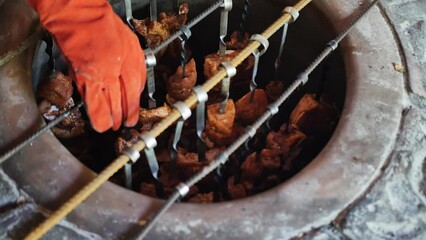 the hands of the kebab cook in a red anti-heat glove lower many skewers with khorovats in a vertical position into the tonir for frying on coals in a stone tandoor. cooking barbecue