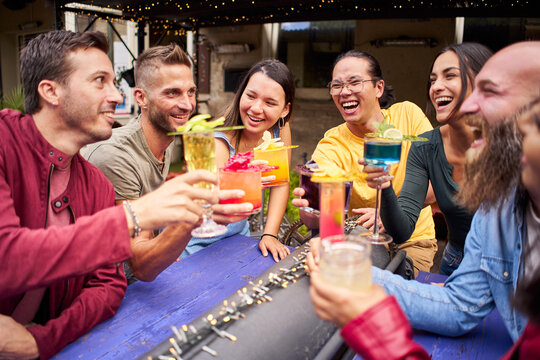 Young people cheers and having fun. Group of happy friends drinking and toasting cocktails at brewery bar terrace pub.