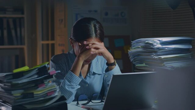 Young Asian office employee feeling tired, fatigue, exhausted while working overtime at night in office