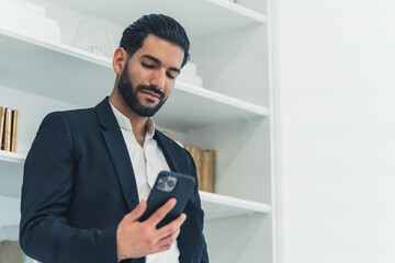 Fototapeta premium young adult Latin freelance businessman using mobile phone checking social media network feed or message chat at home office. Online digital communication, rest after hard work day. High quality photo