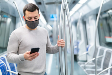 Young man in protective face mask using smartphone while traveling in subway car. Concept of new...