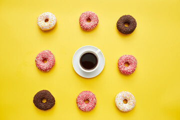 Coffee and sweet doughnuts knolling on yellow background, cup of black coffee in center of treats