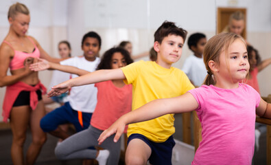Kids of different nationalities working near ballet barre during class in dance school