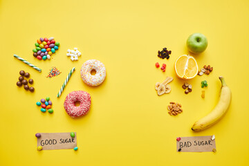 Unhealthy candies and doughnuts and fresh organic fruits and nuts on yellow background with good sugar and bad sugar inscriptions