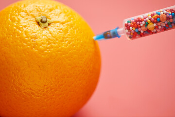 Sugar substitute: close-up of injecting sweet sprinkles into fresh orange using medical syringe