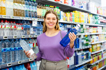 Portrait of female customer buying still water in grocery store, satisfied with purchases