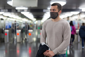 Fototapeta na wymiar Young man in protective face mask walking through underground station, waiting for train. Necessary precautions during coronavirus pandemic