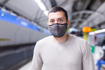 Young man in protective face mask walking through underground station, waiting for train. Necessary precautions during coronavirus pandemic