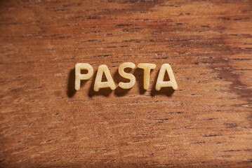 Word pasta formed with alphabet soup pasta letters on a wooden background.