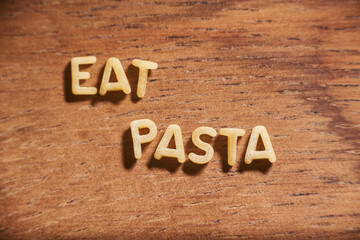 Text eat pasta formed with pasta letters on a wooden background. Italian food.