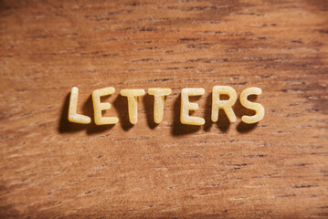 Word Letters formed with alphabet soup pasta letters on a wooden background.