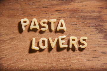 Text Pasta lovers formed with alphabet soup pasta letters on a wooden surface.