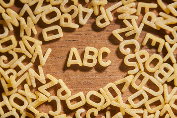 Alphabet soup pasta letters, ABC surrounded by a frame of letters, on wood
