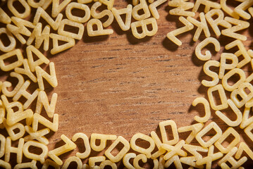 Alphabet soup pasta letters frame on a wooden background. Food and education.
