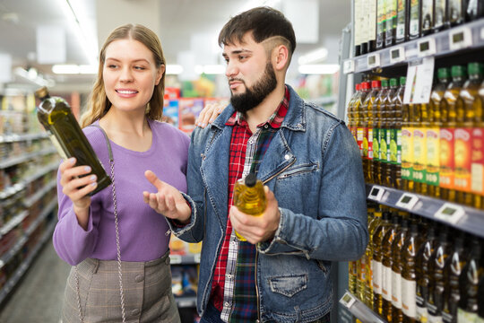 Loving young couple shopping in food shop, choosing bottled vegetable oils - Powered by Adobe